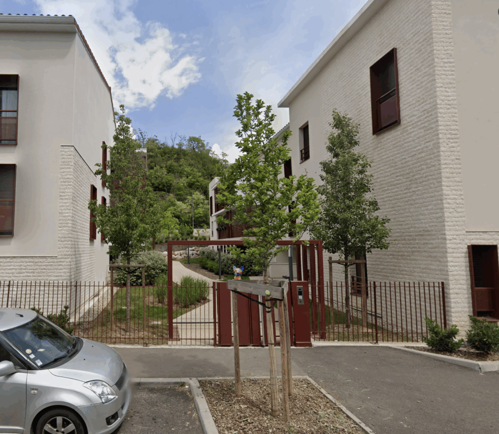 Aménagement paysager des accès, portail en métal et arbres d'ornement en pied de résidence neuve à Feyzin