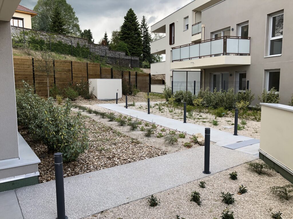 Aménagement paysager du cœur d'îlot résidentiel – Le perchoir paysage Cheminement en béton et massifs plantés dans le cœur d'îlot d'une résidence à Morestel
