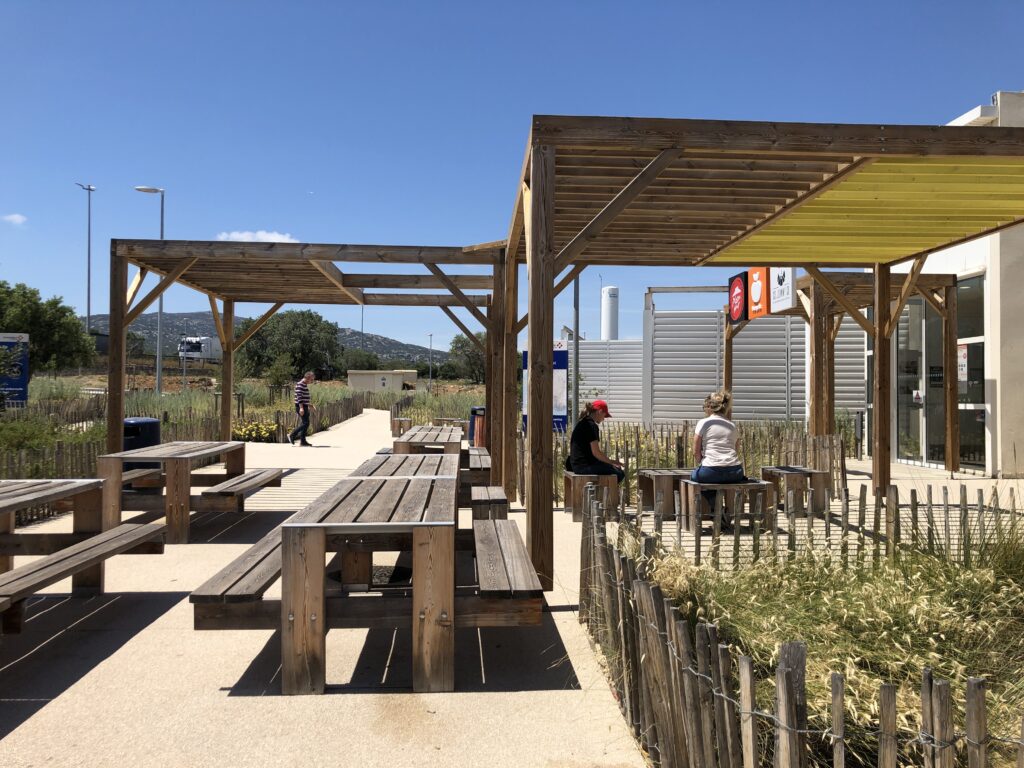 Terrasses d'une aire de repos d'autoroute avec grandes pergolas en bois et tables de pique-nique