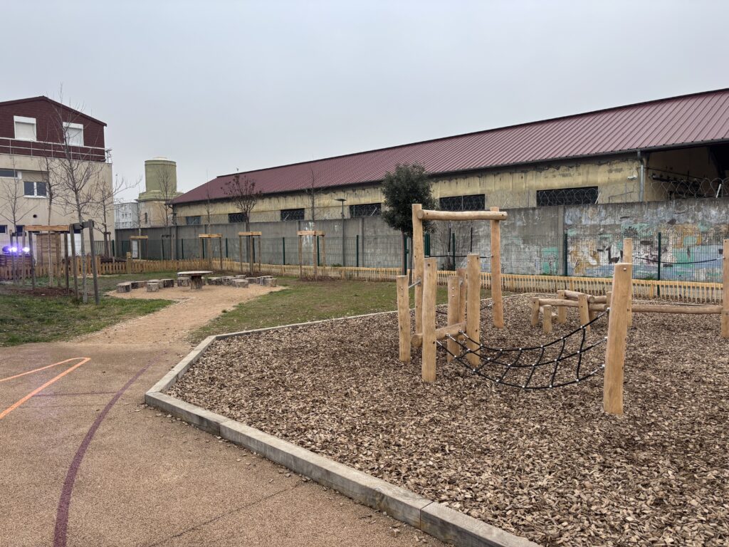 Aménagement d'une classe à ciel ouvert avec gradins en bois et parcours de jeux dans une cour d'école à Saint-Fons